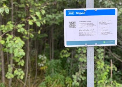 Bilde viser ett nytt informasjonsskilt som henger på en buss stolpe med enkel informasjon til de reisende og en QR kode som kan sende de reisende direkte til Entur  - Klikk for stort bilde